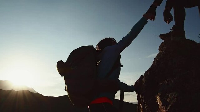 Couple teamwork together help on challenge travel. Helping hand silhouette between two climbers. Man give directions to woman hiker.Teamwork group of tourists lends helping hand to climb cliff rock