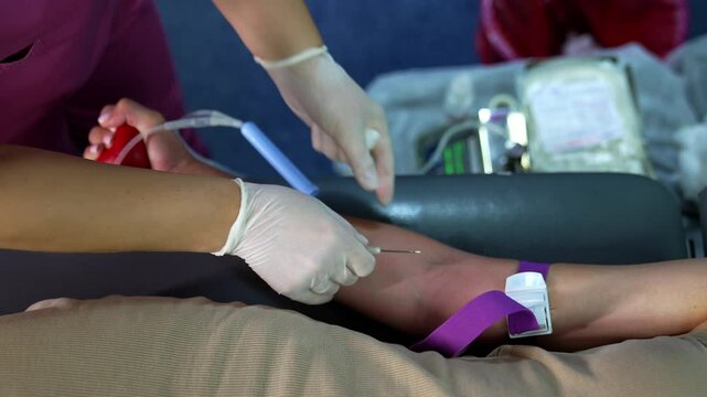 Female hand with a tourniquet on the forearm. Medic inserts a needle into the vein and a drop of blood appears. Donor giving blood.