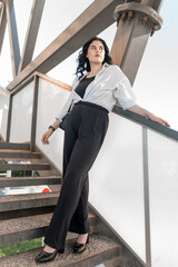 Confident Woman in Professional Attire Posing on Industrial Staircase Under Modern Architecture