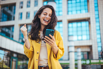 Excited Woman Celebrating Success on Smartphone Outside Modern Building