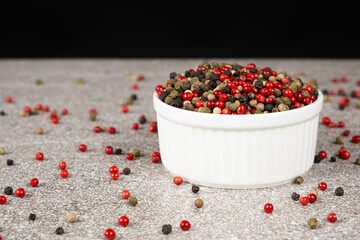 Multicolored peppercorns on a stone gray background.