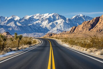 Naklejka premium The photograph presents a Nevada desert highway from a wide-angle perspective, with snow-capped peaks in the distance. The road is empty, surrounded by desert shrubs and a cloudless blue sky.