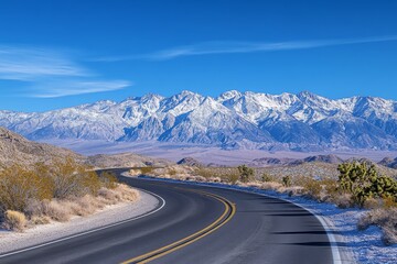 The wide-angle photograph presents a lonely highway in Nevada’s desert, leading towards snow-capped mountains. The road meanders through desert vegetation under a clear, bright blue sky