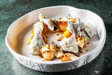 Top view of a gourmet dish featuring seared scallops, peach slices, and garnishes on a white plate, set against a textured grey background. Perfect for culinary and gourmet cuisine themes.