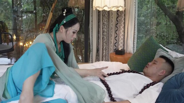 The woman touches the wooden prayer beads on the man's chest, while he continues to rest on the bed.