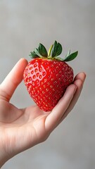 Obraz premium Hand holding a strawberry, focusing on its juicy texture and vibrant color.