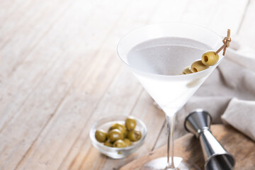 Vodka martini cocktail with vodka and vermouth and green olives on wooden table. Copy space