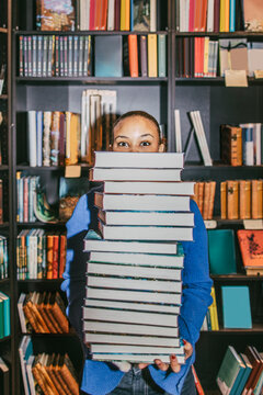 Portrait of young woman holding stack of books while standing in bookstore