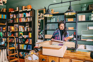 Female owner unpacking new books from cardboard box in store