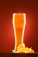 a glass of beer on a wooden stand and potato chips, on a red background, a close-up object, beer bubbles and foam
