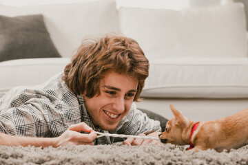 Happy young man playing with his puppy in living room