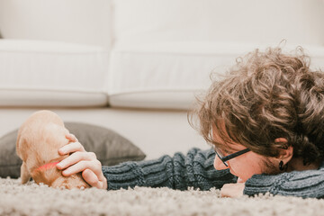 Young man relaxing at home playing with puppy dog