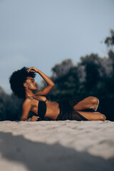 Pretty young african woman posing lying down on sand in beach.