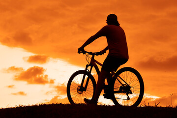 Obraz premium male silhouette of Mountain biker looking at the sunset. man rides up a steep mountain, hill bike trail. Biker on mountain bike adventure against sunset. cloudy sky. unrecognizable person.