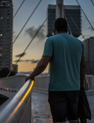 Man crossing a bridge with the sunset on the city © Laia
