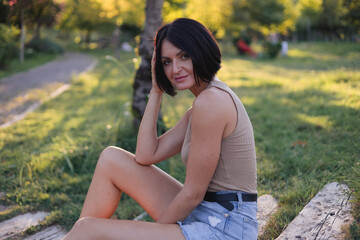 Portrait of a young pretty woman, sitting on a wooden stairs in green public park 