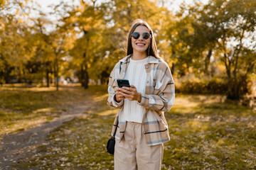 attractive young woman walking in autumn wearing jacket using phone