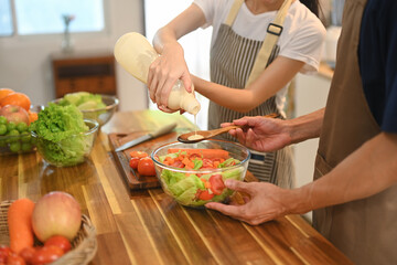 Cheerful young couple preparing healthy vegetable salad in minimal kitchen