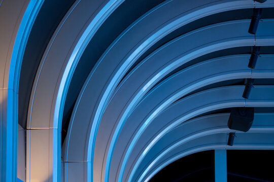 Ceiling with curved blue and white LED strips and suspended directional LED downlights. Modern architecture, interior design and innovative lighting solutions in commercial spaces.