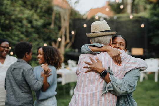 Happy woman greeting senior man during social gathering at garden party