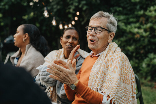 Senior man clapping and enjoying with family members during social gathering at garden party