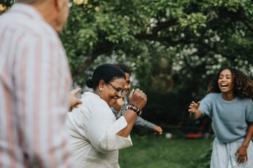 Active senior woman dancing with family members during social gathering at garden party