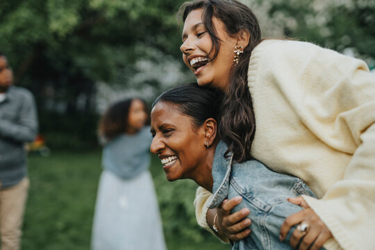 Cheerful mature woman piggybacking daughter at social gathering with family in back yard