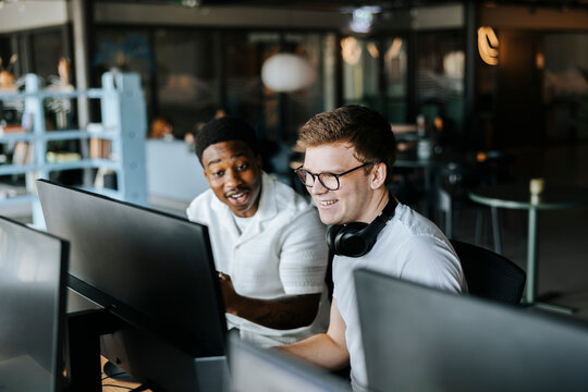 Happy male entrepreneurs watching computer screen while sitting at office