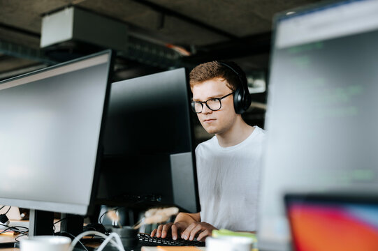 Young male computer programmer typing on desktop PC while sitting on desk in office