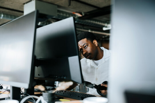Tired male businessman with head in hand looking at computer screen in tech startup office
