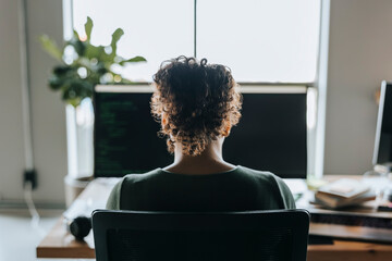 Rear view of female programmer with curly hair coding in tech startup office