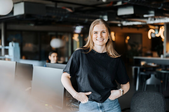 Portrait of smiling female tech professional standing with hands in pockets at office