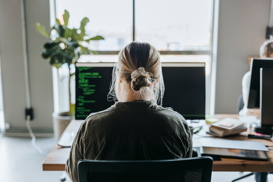 Rear view of female programmer coding on computer while sitting at desk in office