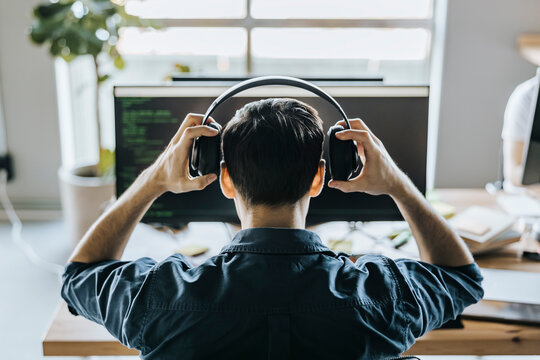 Rear view of male programmer wearing headphones in office
