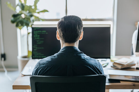 Rear view of male programmer coding while sitting at desk in tech startup office
