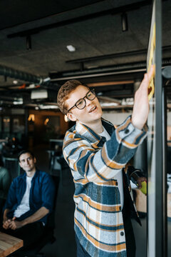 Businessman sticking adhesive notes on whiteboard while conducting meeting in office