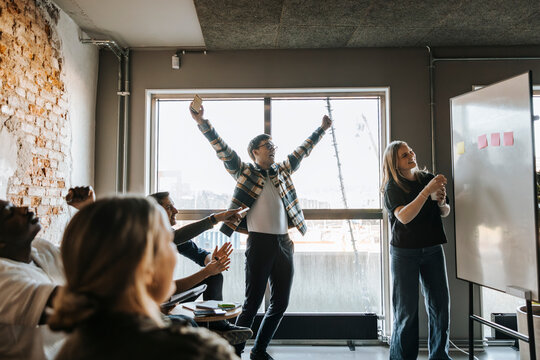 Cheerful computer programmers celebrating during team meeting in tech startup office