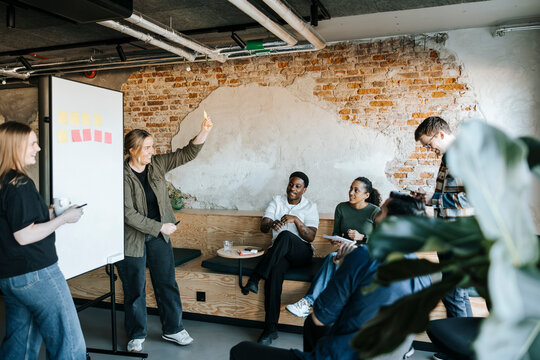 Female tech programmer showing adhesive note to happy colleagues in business meeting at office