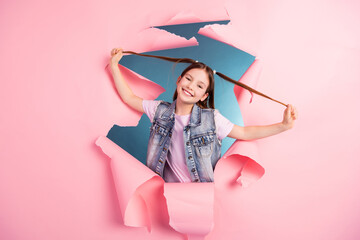 Photo portrait of charming little girl have fun pull tails ripped paper poster wear trendy jeans outfit isolated on blue color background