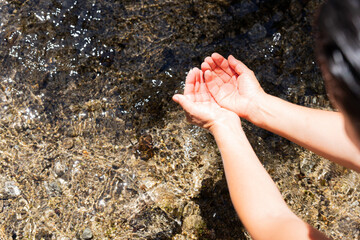 Top view of a female hikers arms collecting water between her hands from a crystal-clear, high mountain stream