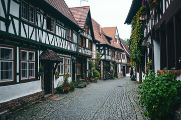Obraz premium A charming cobblestone street winds through a quaint German village, lined with traditional half-timbered houses adorned with vibrant greenery.