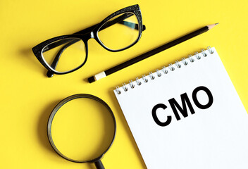 A notebook with CMO written on it placed next to a pair of glasses, symbolizing a business concept related to a Chief Marketing Officer.