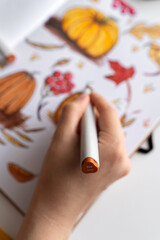 Hand holding marker while drawing autumn illustration