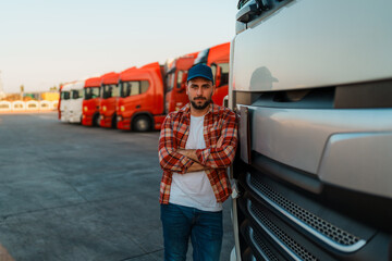 Smiling owner of transportation posing for photo on a truck parking lot with several trucks in the...