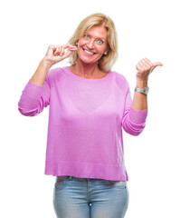 Middle age blonde woman eatin pink macaron biscuit over isolated background pointing and showing...