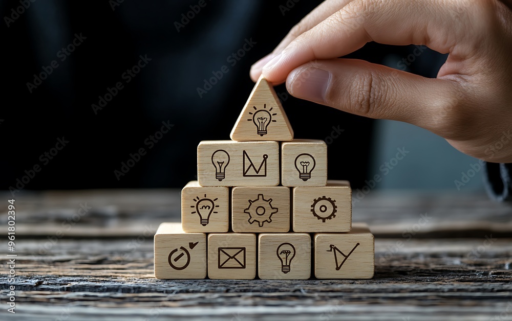 Wall mural building innovation pyramid - hand arranging wooden tiles with lightbulb and gear icons for strategi