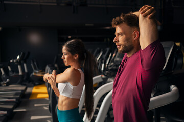 A side view of athletic young adult man and woman stretching at the gym