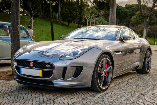 Elegant Jaguar F-type coupe car parked on cobblestone road near park