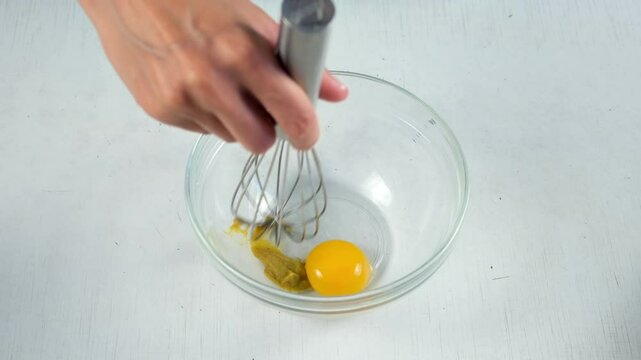 Woman preparing homemade mayonnaise whisking mustard with egg yolks in glass bowl, hands close-up. Cooking sauce for salad, meat dishes. Dressing for different dishes. Culinary, cuisine concept.