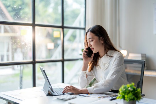 Young asian businesswoman talking on phone and using digital tablet at work